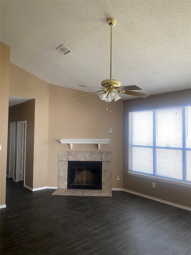 Unfurnished living room featuring dark wood finished floors, a fireplace, a textured ceiling, vaulted ceiling, and ceiling fan