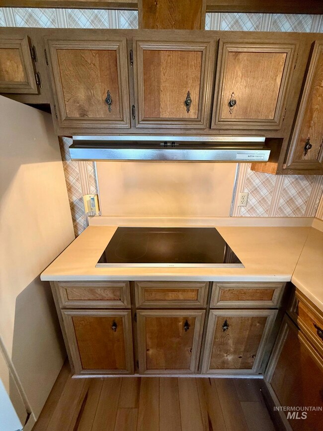 Kitchen view of black electric stovetop, light countertops, wood finished floors, and backsplash