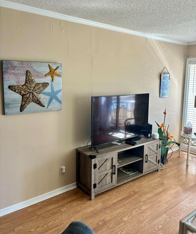 Living room featuring ornamental molding, a textured ceiling, and light hardwood / wood-style floors
