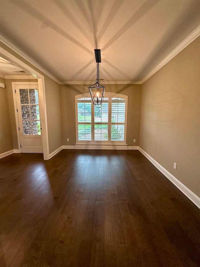 Spare room featuring dark wood-type flooring, baseboards, and crown molding