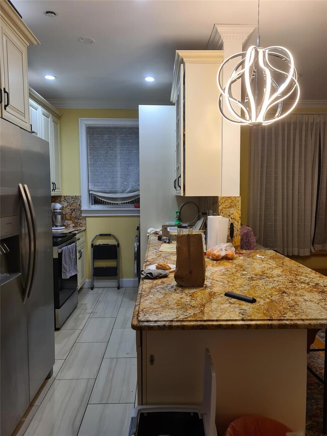 Kitchen with ornamental molding, stainless steel refrigerator with ice dispenser, decorative backsplash, range with electric cooktop, and a chandelier