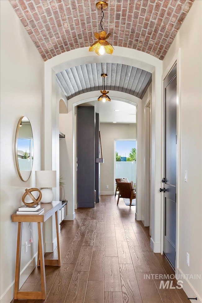 Corridor featuring arched walkways, hardwood / wood-style floors, brick ceiling, and vaulted ceiling