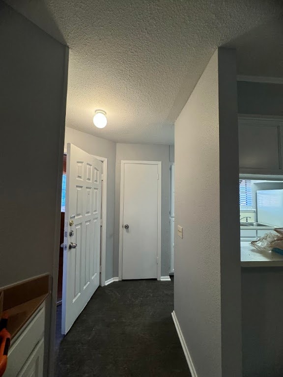 Hall with a textured ceiling, dark carpet, and bas