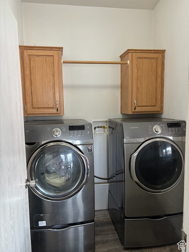 Washroom featuring cabinet space, dark wood-type flooring, and washing machine and clothes dryer