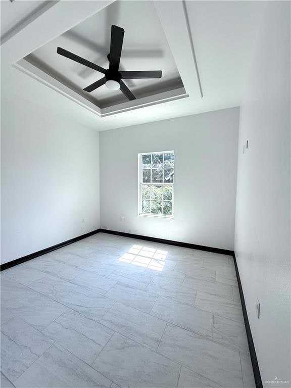 Unfurnished room featuring a tray ceiling, baseboards, ceiling fan, and marble look tiles