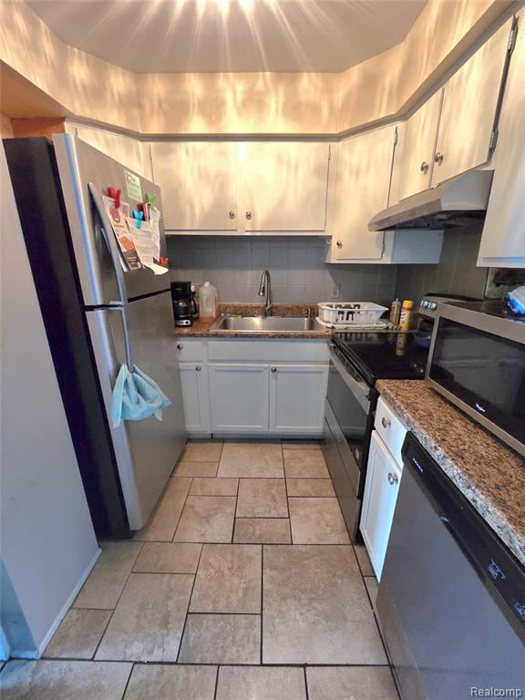 Kitchen with backsplash, stainless steel appliances, under cabinet range hood, light tile patterned flooring, and dark stone countertops