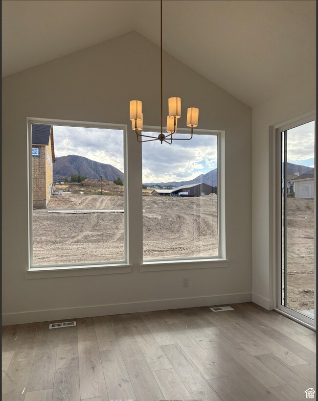 Unfurnished dining area featuring a mountain view, light wood-style flooring, lofted ceiling, and a chandelier