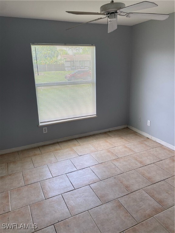 Tiled empty room featuring ceiling fan and baseboa
