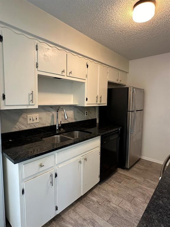 Kitchen with light wood-style flooring, dark stone countertops, decorative backsplash, black dishwasher, and a textured ceiling