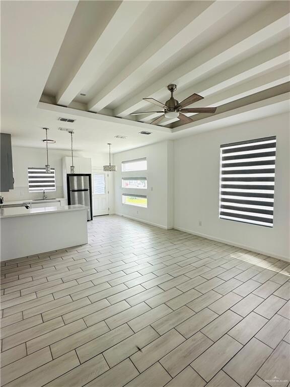 Unfurnished living room with visible vents, a ceiling fan, a sink, beamed ceiling, and baseboards