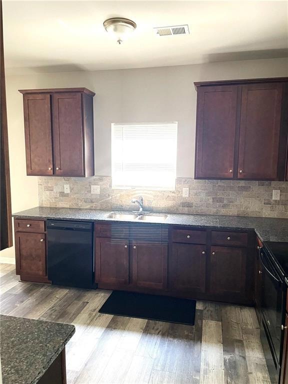 Kitchen with black appliances, light wood finished floors, decorative backsplash, and dark stone counters