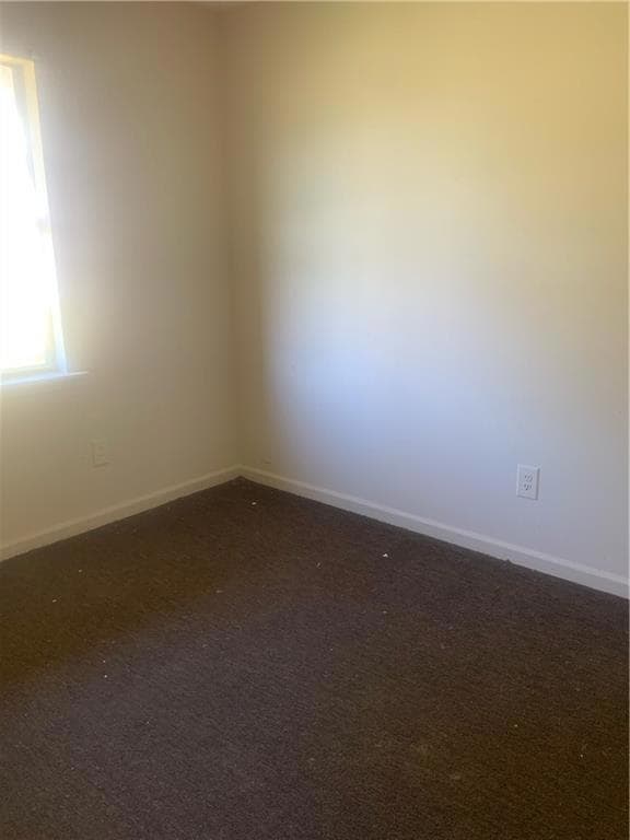 Unfurnished room with dark colored carpet and base