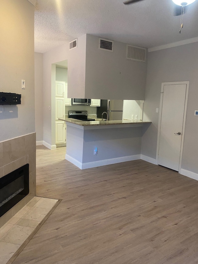 Kitchen featuring light wood-type flooring, a peninsula, refrigerator, stainless steel range, and light stone counters