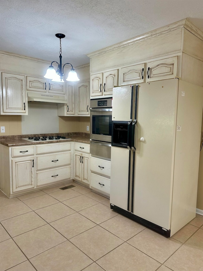 Kitchen featuring white fridge with ice dispenser, a textured ceiling, light tile patterned flooring, dark countertops, and pendant lighting