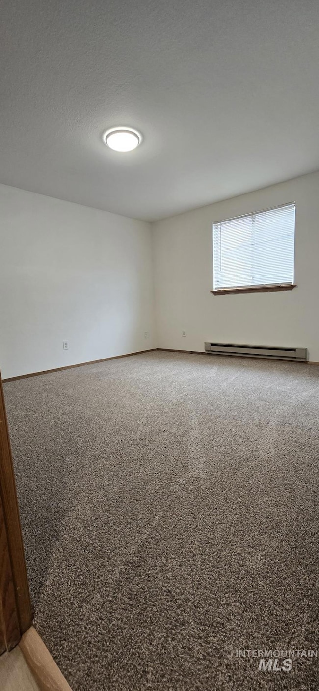Spare room with a textured ceiling, light carpet, and a baseboard radiator