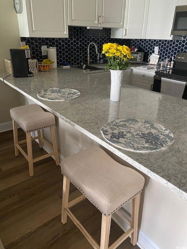 Kitchen featuring decorative backsplash, stainless steel microwave, black electric range oven, a kitchen bar, and a sink