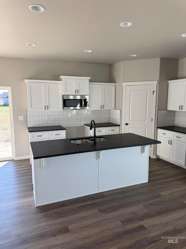 Kitchen featuring tasteful backsplash, an island with sink, recessed lighting, stainless steel microwave, and dark wood-type flooring
