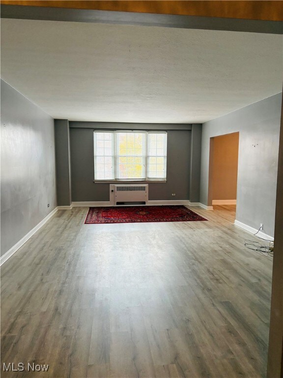 Empty room featuring wood type
 floors and radiator