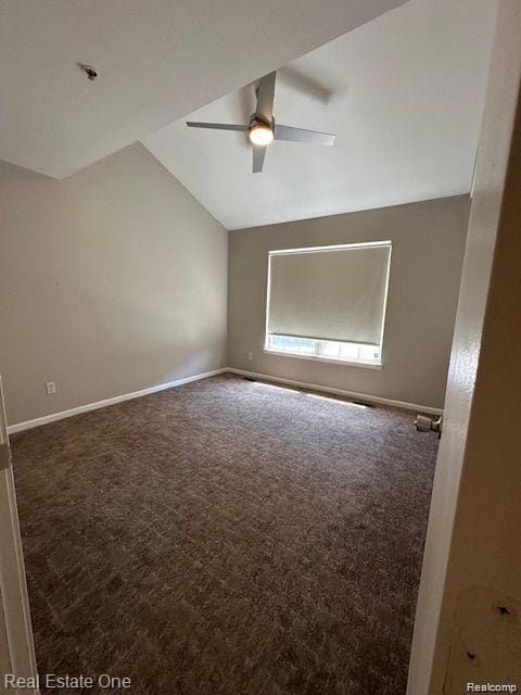 Spare room featuring dark colored carpet, lofted ceiling, and a ceiling fan