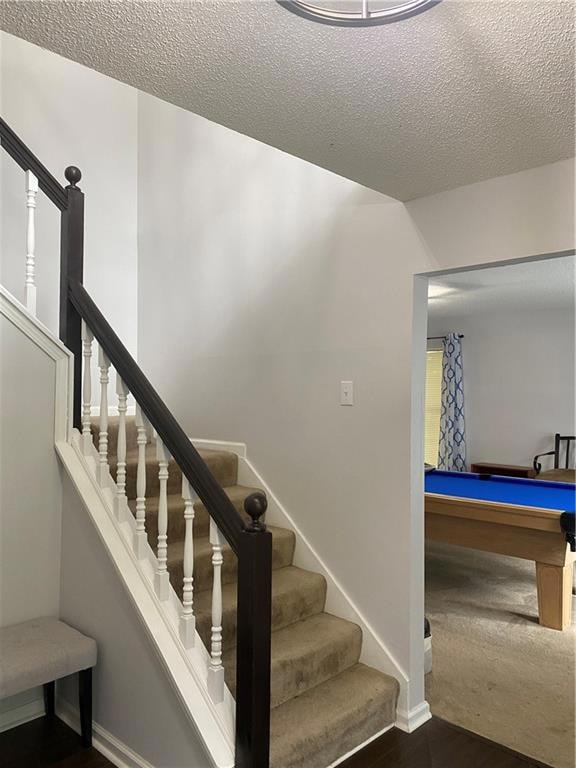 Staircase with pool table, baseboards, a textured 