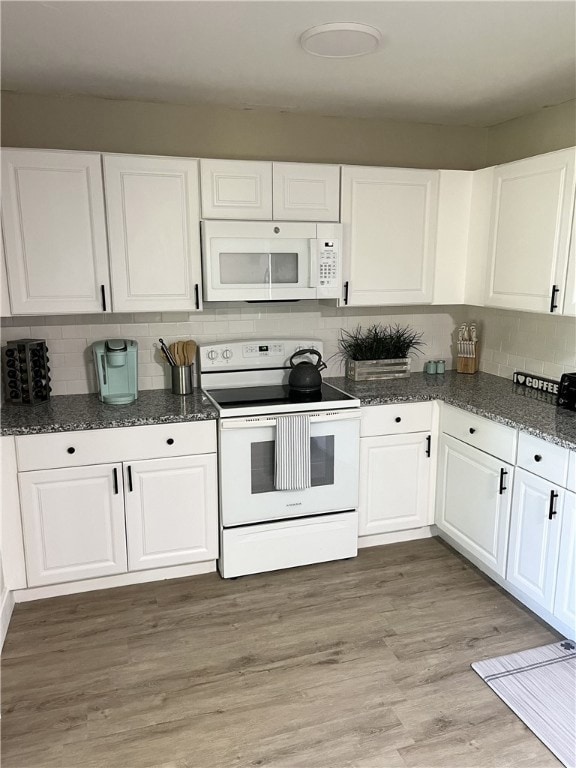Kitchen with white appliances, white cabinets, light wood-type flooring, and dark stone counters