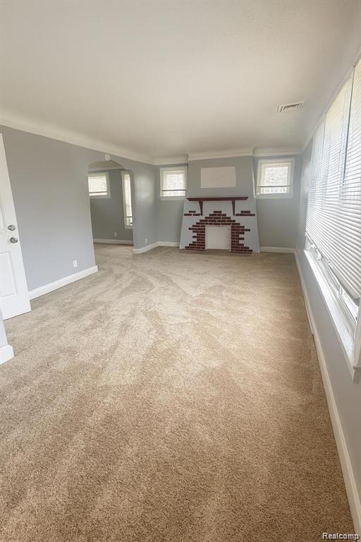 Unfurnished living room with light colored carpet, arched walkways, ornamental molding, and a fireplace