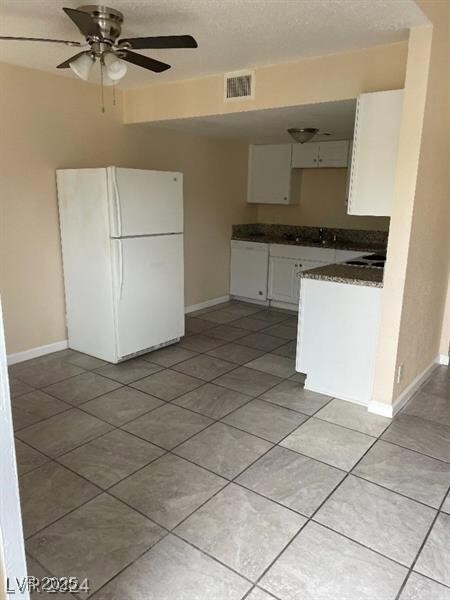 Kitchen featuring white appliances, dark countertops, white cabinets, baseboards, and a textured ceiling