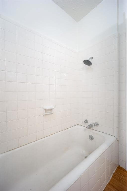 Full bath featuring wood finished floors, a textured ceiling, and washtub / shower combination
