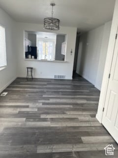 Unfurnished dining area featuring dark wood-type flooring and a chandelier