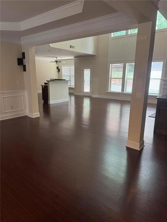 Unfurnished living room featuring ornamental molding, dark wood-style floors, and a ceiling fan