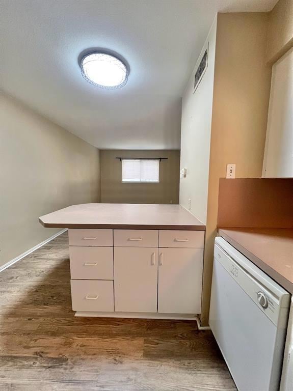 Kitchen with wood finished floors, white dishwasher, a peninsula, light countertops, and white cabinetry