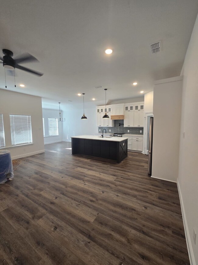 Kitchen featuring open floor plan, glass insert cabinets, hanging light fixtures, light countertops, and a kitchen island with sink