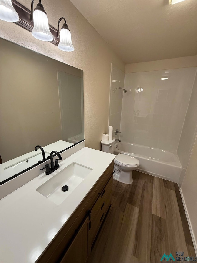 Full bath with a textured wall, dark wood-style flooring, vanity, and washtub / shower combination