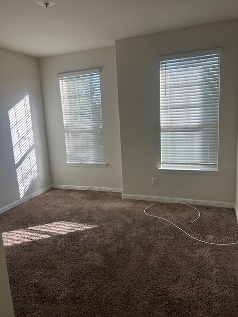 Spare room with healthy amount of natural light and dark colored carpet
