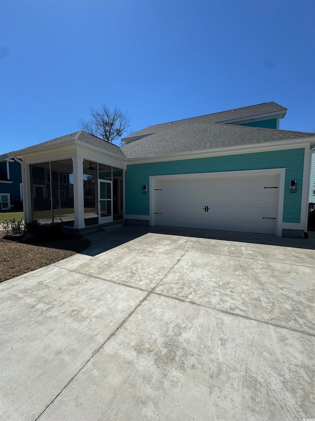 View of front facade featuring roof with shingles, a sunroom, a garage, and concrete driveway