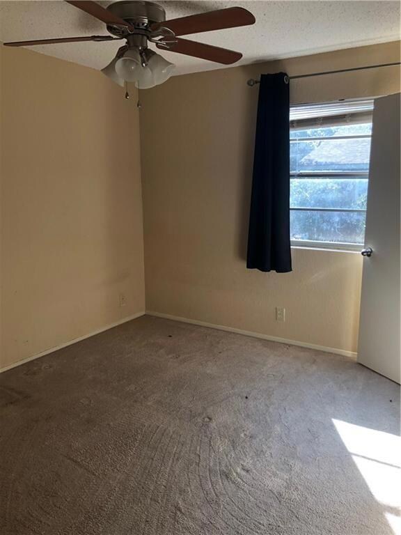 Carpeted empty room with a ceiling fan, baseboard