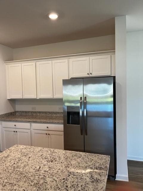 Kitchen with stainless steel refrigerator with ice dispenser, white cabinets, dark wood-style flooring, light stone countertops, and recessed lighting