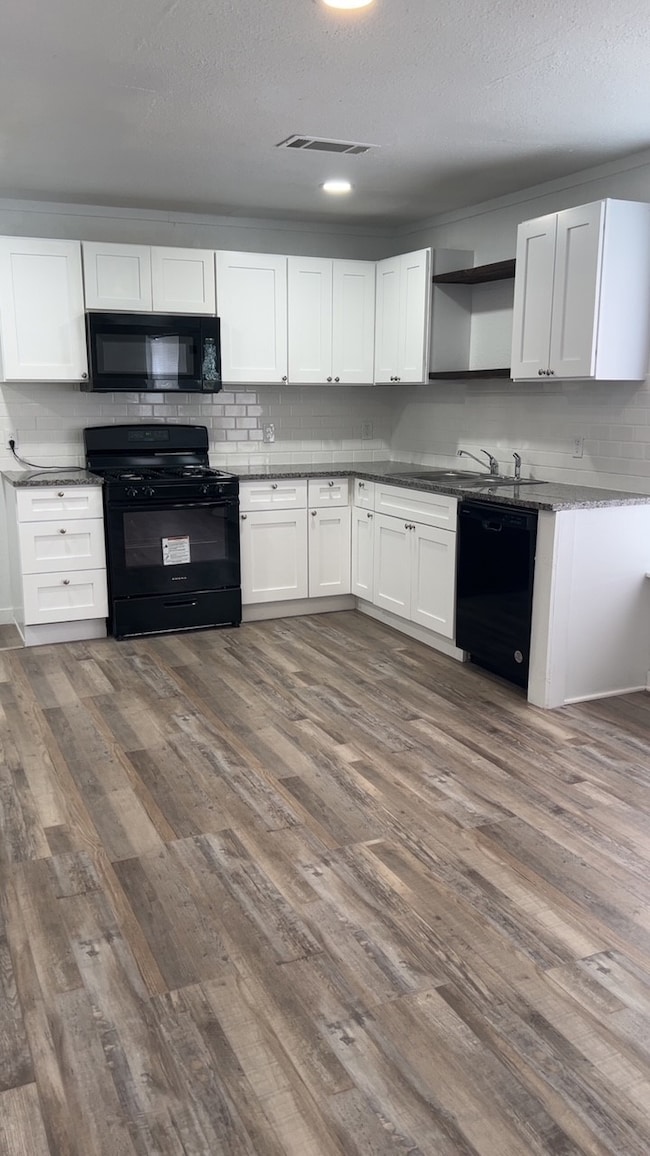 Kitchen featuring black appliances, white cabinets, backsplash, dark wood-type flooring, and a textured ceiling