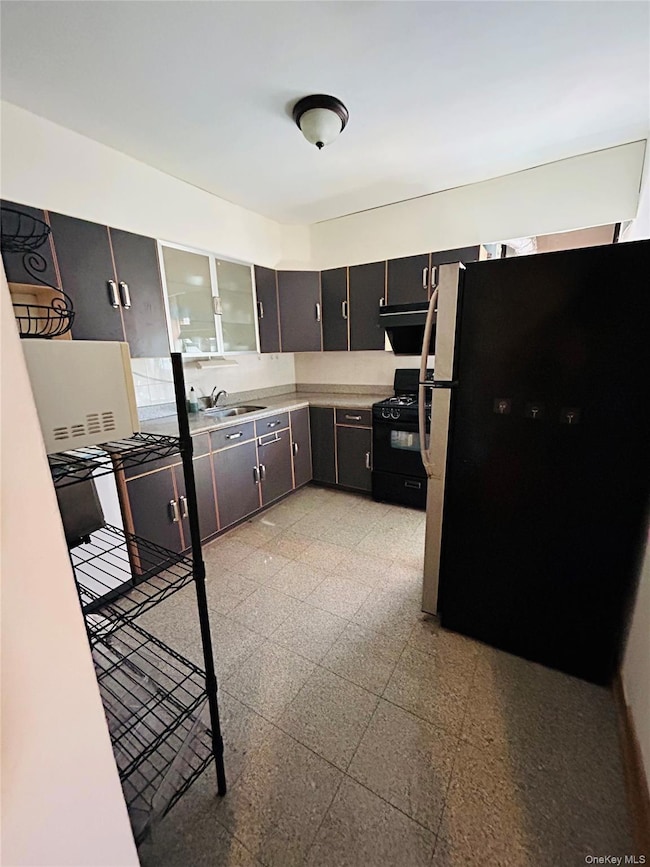 Kitchen with freestanding refrigerator, light flooring, black gas range oven, light countertops, and glass insert cabinets
