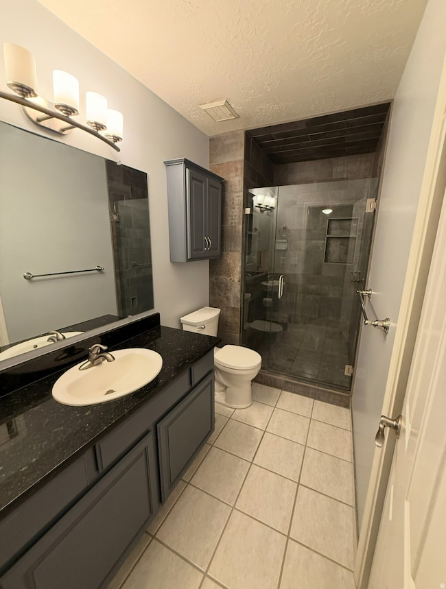Full bathroom featuring a shower stall, a textured ceiling, vanity, and light tile patterned flooring