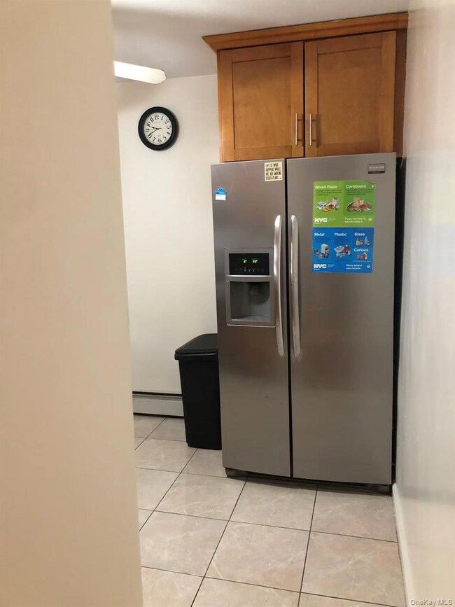 Kitchen with stainless steel fridge with ice dispenser, light tile patterned floors, brown cabinetry, and a baseboard radiator