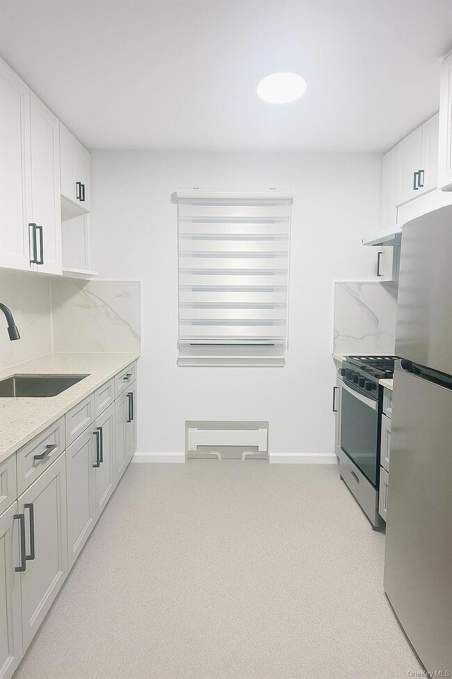 Kitchen with light carpet, white cabinetry, stainless steel appliances, light stone countertops, and backsplash