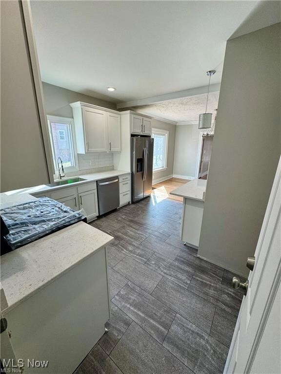 Kitchen featuring light countertops, white cabinets, appliances with stainless steel finishes, pendant lighting, and backsplash