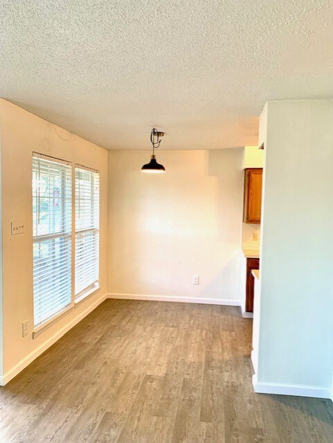 Empty room with a textured ceiling, baseboards, and wood finished floors