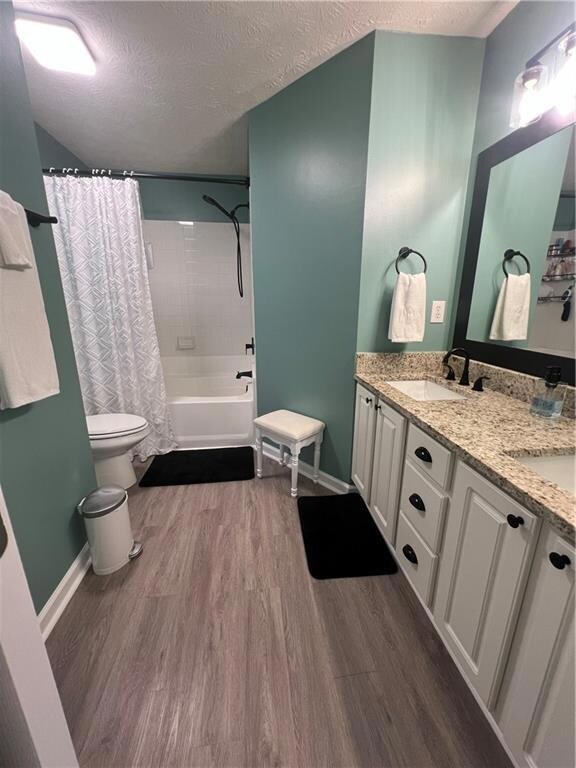 Full bath with toilet, wood finished floors, a textured ceiling, double vanity, and shower / tub combo with curtain
