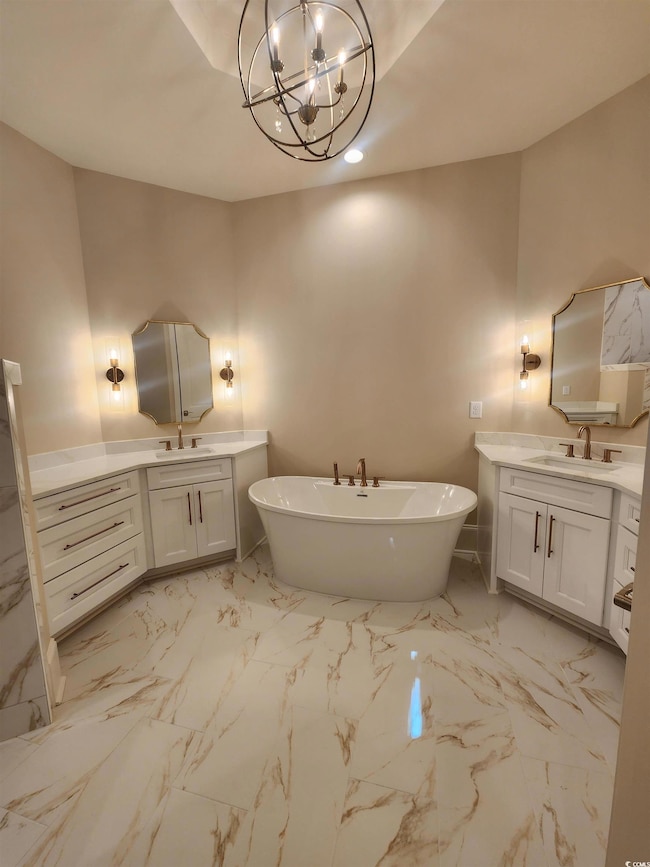 Full bathroom featuring light marble finish floors, two vanities, and a freestanding tub