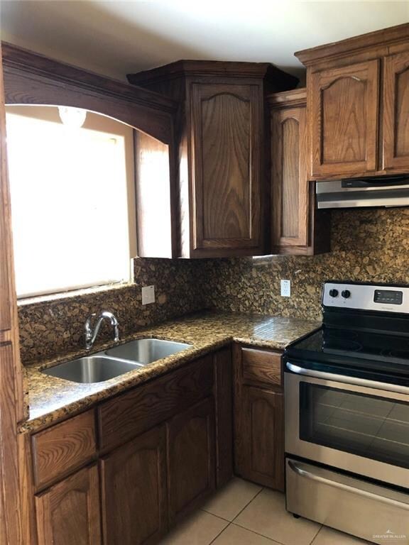 Kitchen featuring stainless steel range with electric stovetop, under cabinet range hood, a sink, tasteful backsplash, and light tile patterned flooring