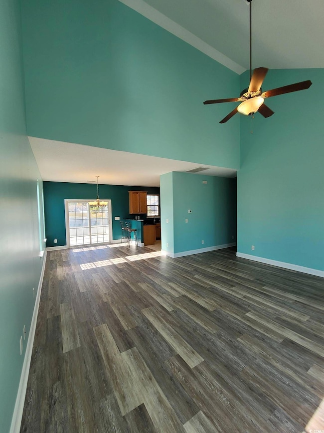 Unfurnished living room featuring dark wood finished floors, high vaulted ceiling, ceiling fan, and a chandelier