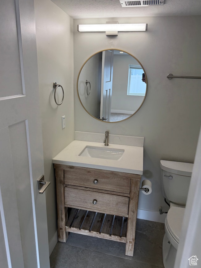 Half bathroom featuring vanity, dark tile patterned floors, and a textured ceiling
