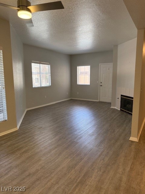 Unfurnished living room featuring dark wood-style floors, a ceiling fan, a textured ceiling, and a tiled fireplace
